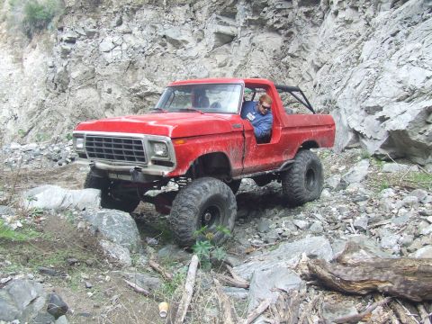 1978 Ford Bronco - A red 1978 Ford Bronco is shown off-roading on a rocky, mountainous terrain.