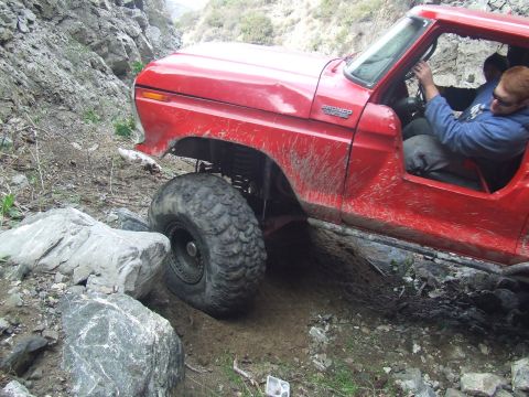1978 Ford Bronco - A red off-road vehicle with large tires is seen navigating a challenging rocky path.