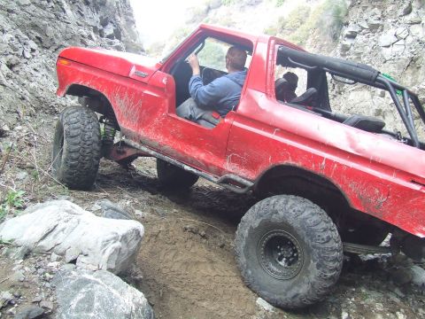 1978 Ford Bronco - A red 1978 Ford Bronco tackles a challenging off-road trail with steep, rocky inclines.