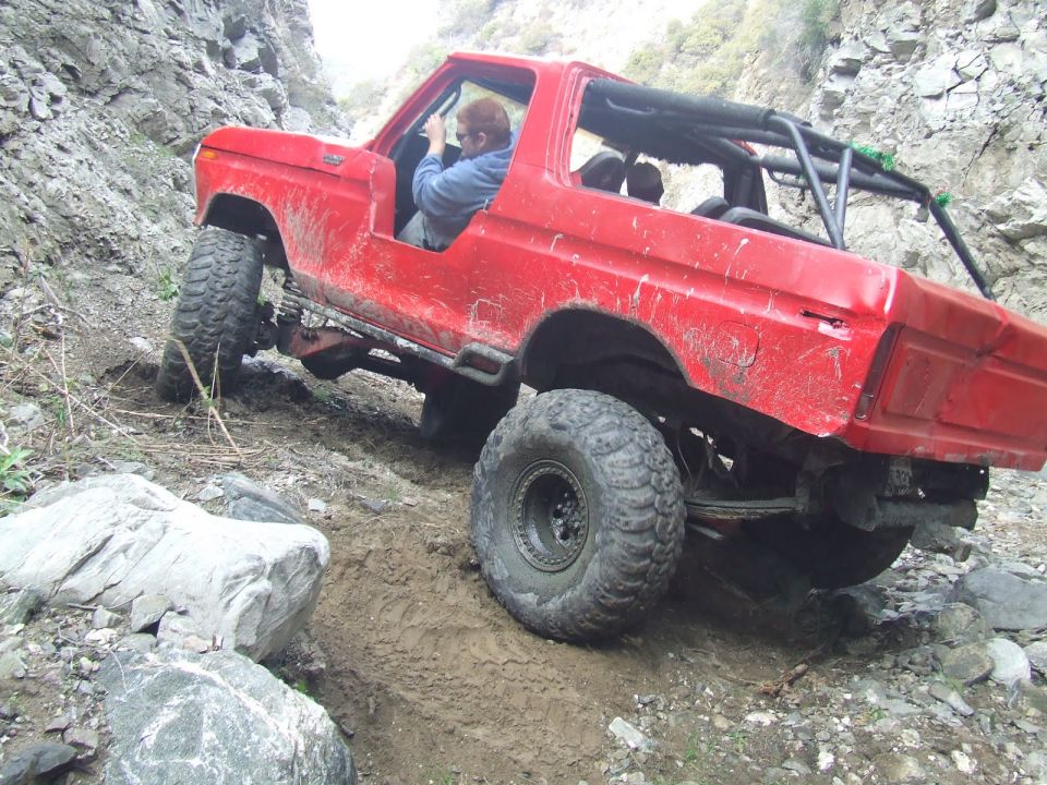 1978 Ford Bronco climbing a steep, rocky, dirt trail with large tires and a roll cage
