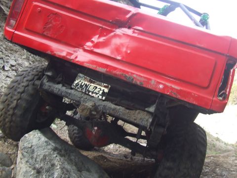 1978 Ford Bronco - This red off-road vehicle is shown from the rear, with significant body damage, navigating a challenging rocky path.