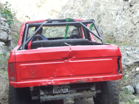 1978 Ford Bronco - A red 1978 Ford Bronco navigates a rocky off-road path, showing damage to its rear.