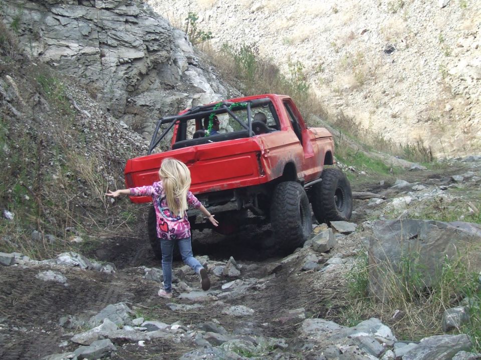 Red 1978 Ford Bronco modified for off-roading, with roll cage and oversized tires, climbing a rocky trail
