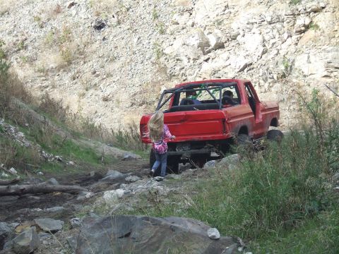 1978 Ford Bronco - A red 1978 Ford Bronco navigates a rough, rocky terrain with a young girl observing.