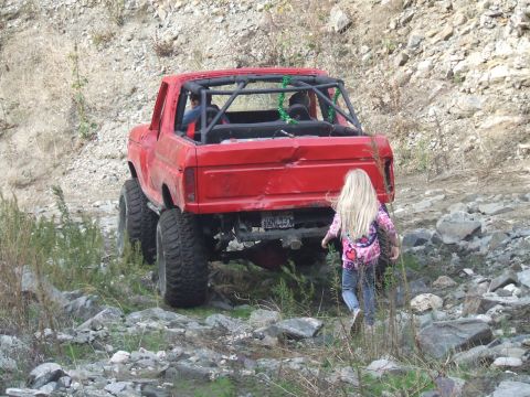 1978 Ford Bronco - A red 1978 Ford Bronco with a roll cage is parked in a rocky outdoor area, with a young girl walking nearby.