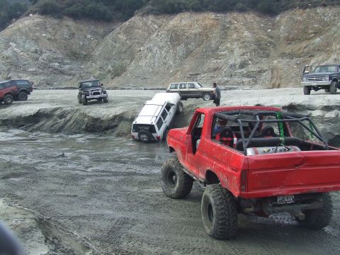 1978 Ford Bronco - A red 1978 Ford Bronco with a roll cage navigates a muddy off-road course alongside other vehicles.