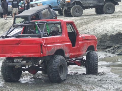1978 Ford Bronco - Muddy 1978 Ford Bronco navigating a rough terrain with other vehicles in the background.