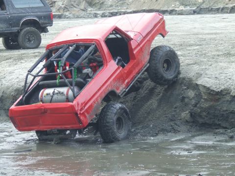 1978 Ford Bronco - A modified red Bronco navigates a challenging off-road obstacle, with another vehicle visible in the background.