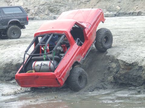 1978 Ford Bronco - A red 1978 Ford Bronco navigates a challenging muddy terrain, with another vehicle visible in the background.