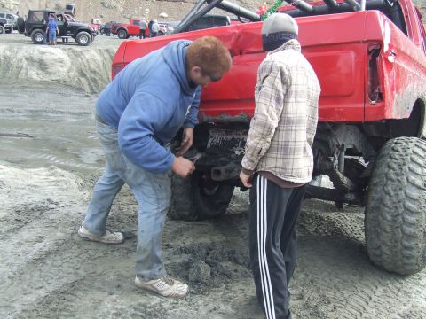 1978 Ford Bronco - Two people inspect the rear of a heavily modified red truck in a muddy, off-road environment.