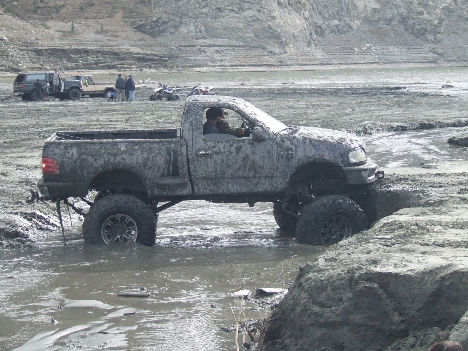 Mud-covered pickup truck with lifted suspension stuck in mud