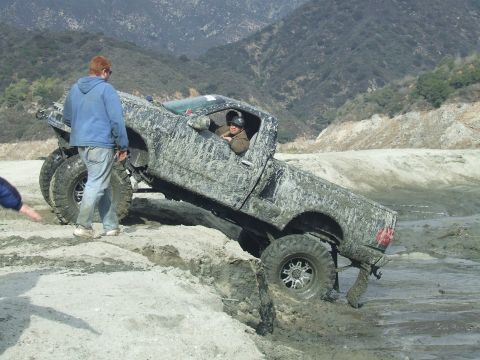 1978 Ford Bronco - A heavily mud-splattered pickup truck navigates a challenging off-road terrain, getting stuck in a muddy rut.