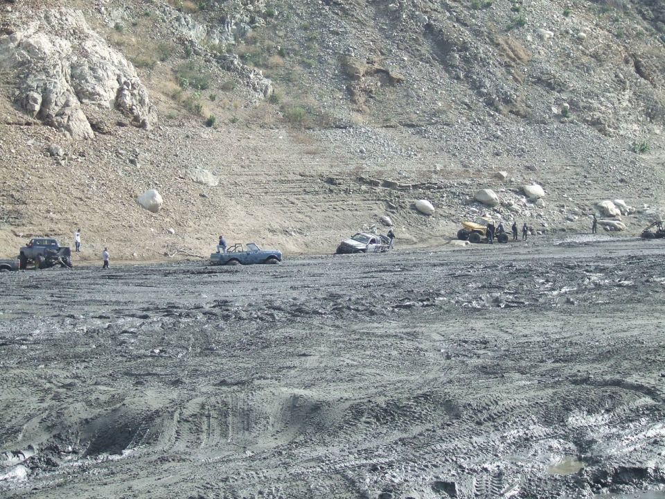 Several off-road vehicles stuck in mud with people around them