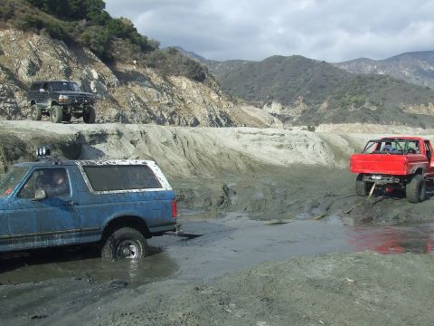 1978 Ford Bronco - Multiple off-road vehicles navigate a muddy terrain in a canyon.