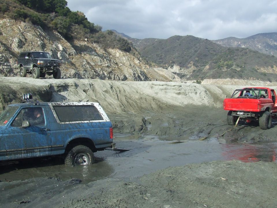 Blue SUV stuck in mud with a red truck nearby