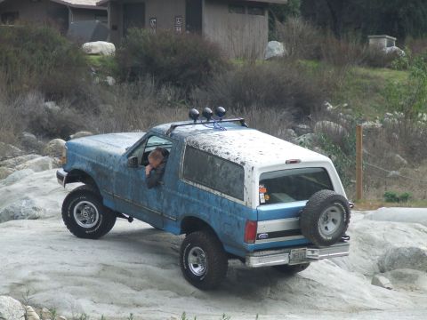 1978 Ford Bronco - A lifted Ford Bronco navigates a rocky terrain, with a driver visible through the window.