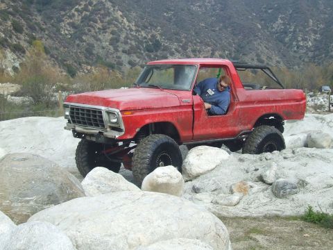 1978 Ford Bronco - A red 1978 Ford Bronco is driven over large rocks in a canyon.