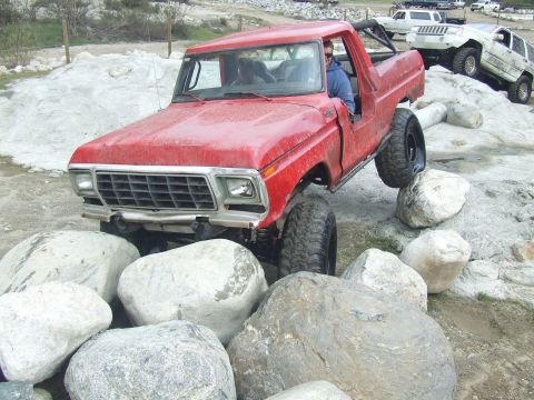 1978 Ford Bronco - A red 1978 Ford Bronco is shown off-roading over large boulders, with other vehicles visible in the background.