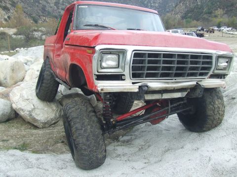 1978 Ford Bronco - This red off-road vehicle is navigating a rocky terrain with its front tires elevated.