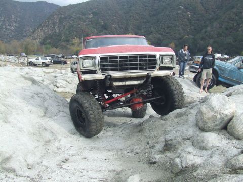 1978 Ford Bronco - A red 1979 Ford F-Series truck navigates a rocky obstacle course, with other vehicles and spectators in the background.