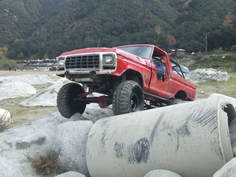 1978 Ford Bronco - A red 1978 Ford Bronco is shown off-roading over large rocks and concrete pipes in a dry, hilly area.