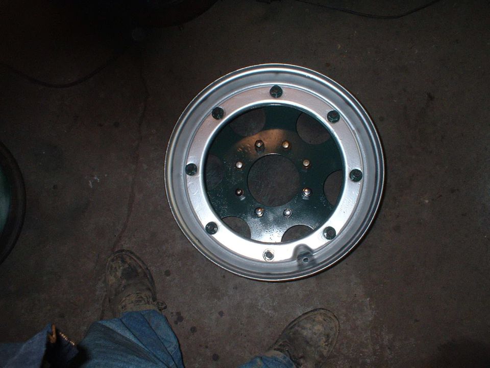 Bare 6-lug steel wheel with silver outer ring and green center lying on a shop floor