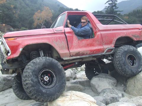 1978 Ford Bronco - This heavily modified SUV is shown off-roading over large rocks in a mountainous area.