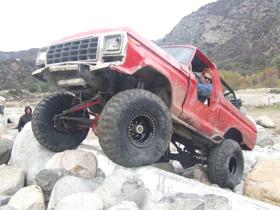 Red 1978 Ford Bronco with large off-road tires navigating rocks