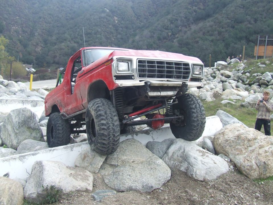 Red 1978 Ford Bronco with large tires climbing over rocks