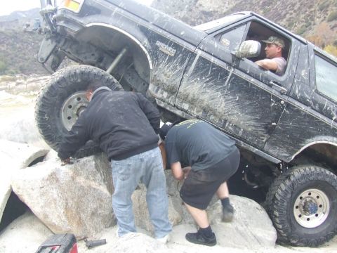 1978 Ford Bronco - A black Ford Bronco is stuck on rocks with two people attempting to free it.
