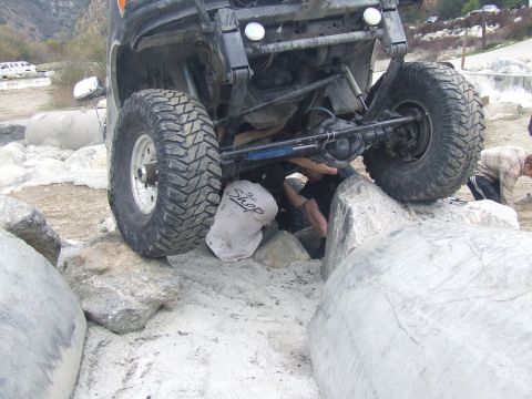 1978 Ford Bronco - People work on the undercarriage of a modified off-road vehicle navigating a rocky terrain.