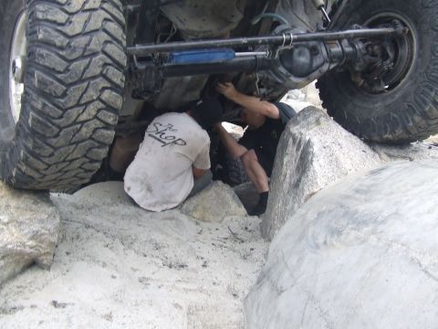 1978 Ford Bronco - Mechanics work on the undercarriage of a large off-road vehicle stuck on rocks.