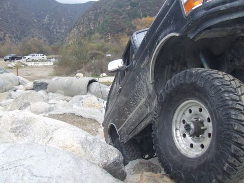 1978 Ford Bronco - A black Ford Bronco is shown navigating a rocky terrain, with other vehicles visible in the background.