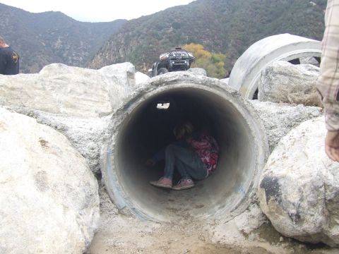 1978 Ford Bronco - A person sits inside a large concrete drainage pipe in a outdoor setting, with an ATV visible on top.