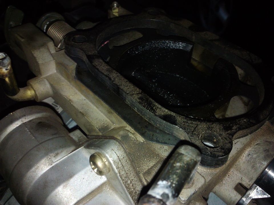 Close-up of a dirty throttle body gasket with metal components and hoses
