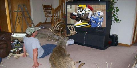 1994 Jeep Cherokee - Man and taxidermied deer watch a football game together in a living room.