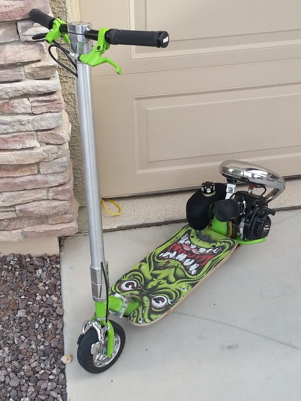 Gas-powered scooter with a skateboard deck a green monster graphic, chrome exhaust, and a small engine