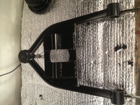 1965 Ford Mustang - A close-up view of a black automotive control arm, likely a replacement part, against a reflective background.
