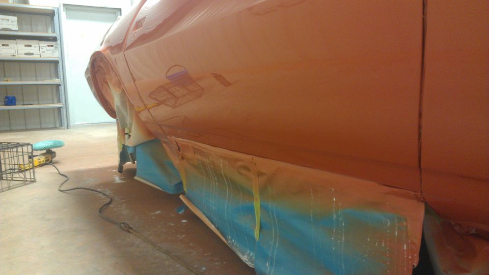 Orange car body side, masked for painting, with reflections of a wire cage