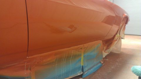 1973 Chevrolet Camaro - Side panel of an orange vehicle is covered in masking tape, possibly during a repair or painting process.