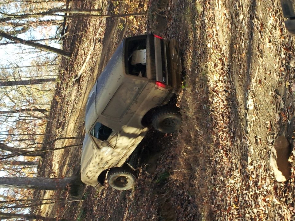 Muddy SUV tilted on a wooded trail, showing its side and front quarter