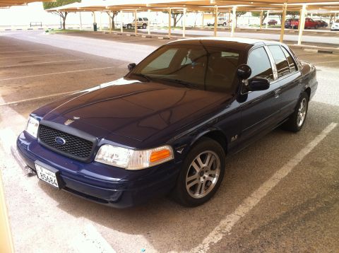 2007 Ford Crown Victoria - A dark blue 2007 Ford Crown Victoria is parked in a lot under a covered walkway.