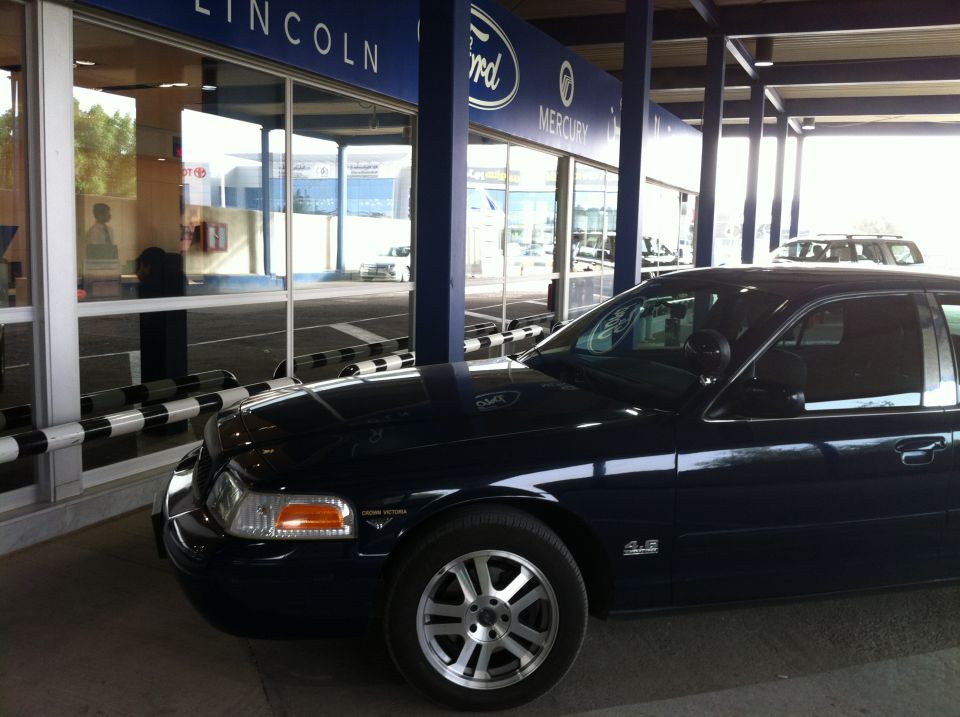 Dark blue 2007 Ford Crown Victoria sedan, front passenger side view, parked in front of a dealership