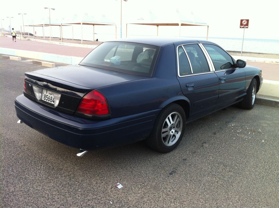 Dark blue 2007 Ford Crown Victoria parked on asphalt near a waterfront promenade