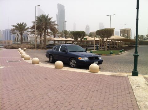 2007 Ford Crown Victoria - A dark blue 2007 Ford Crown Victoria is parked in front of a covered parking area with palm trees and a city skyline visible.