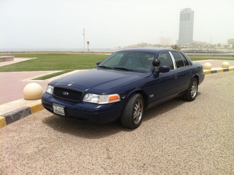 2007 Ford Crown Victoria - Dark blue 2007 Ford Crown Victoria parked near a waterfront promenade with a city skyline in the distance.