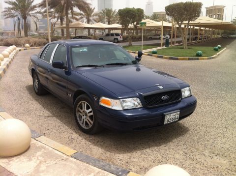 2007 Ford Crown Victoria - A dark blue 2007 Ford Crown Victoria is parked in an outdoor lot with covered parking and palm trees.