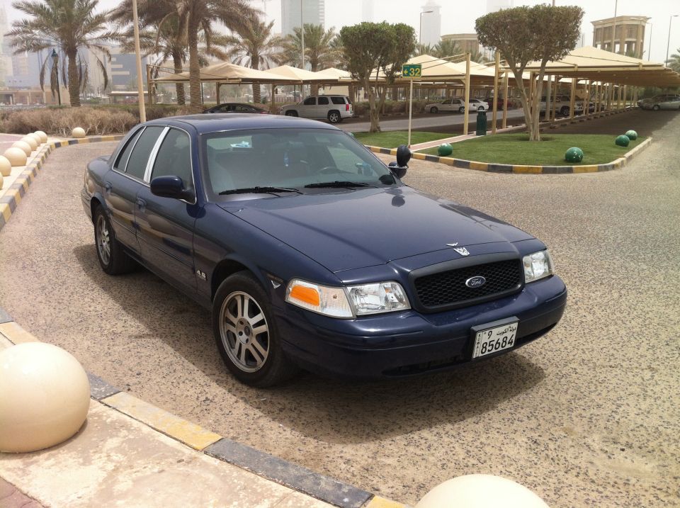 Dark blue 2007 Ford Crown Victoria parked outside with palm trees and buildings in the background