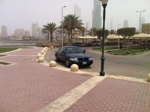 2007 Ford Crown Victoria - A 2007 Ford Crown Victoria is parked near a waterfront promenade with a modern city skyline visible in the distance.