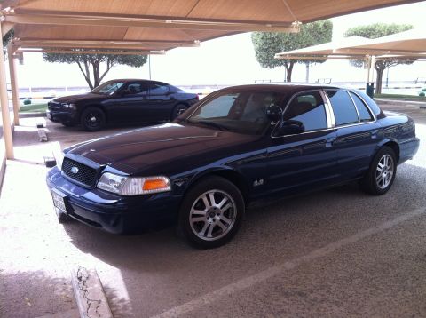 2007 Ford Crown Victoria - A dark blue 2007 Ford Crown Victoria is parked under a canopy next to another dark sedan.